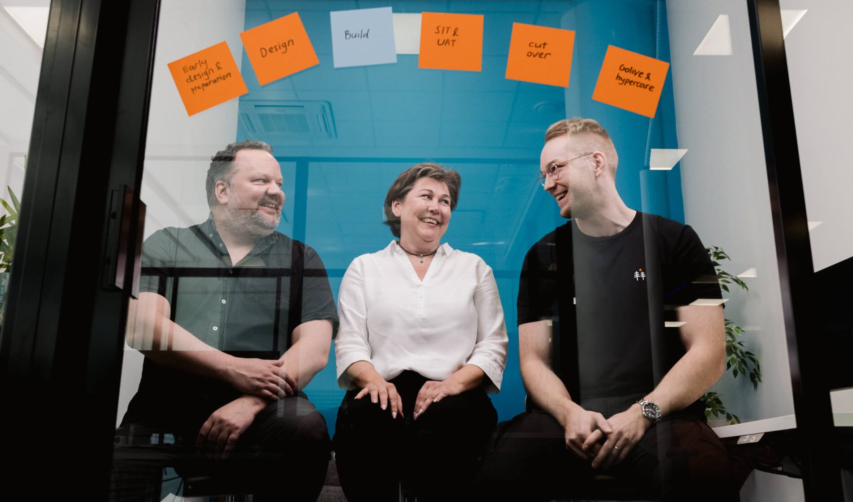 Tiia Vainionpää, Patrik Koso ja Ari Varjonen lasineukkarissa, jonka seinällä muistilapuilla projektin vaiheet.